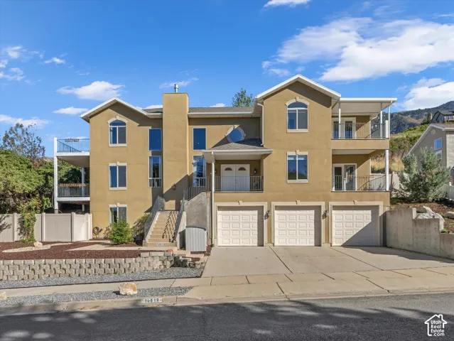 Modern multi-level residence featuring a warm tan exterior with blue accent trim, three-car garage with paneled doors, and architectural detailing including peaked rooflines and varied window styles