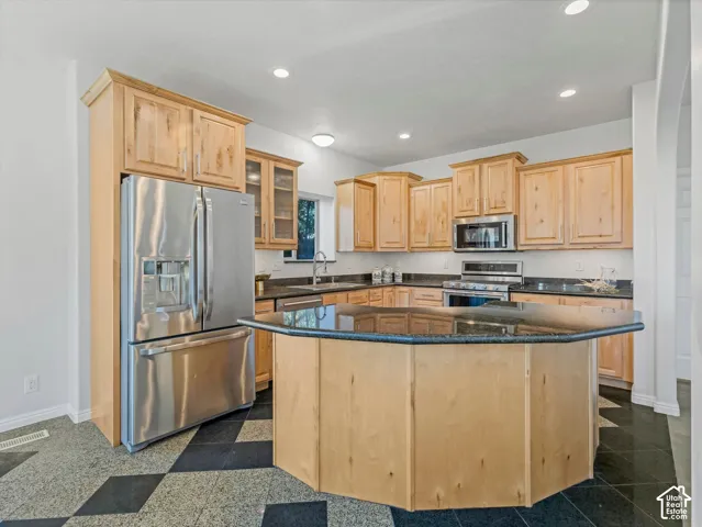 Kitchen featuring light wood cabinetry, dark countertops, stainless steel appliances, and a central island with a multi-sided design