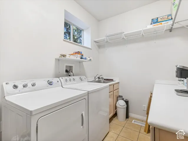Utility room with a sink, light wood-finish cabinetry, and tiled flooring