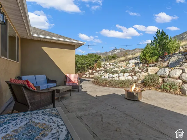 Paved patio area featuring a mounted exterior light fixture, string lights, and a stone retaining wall