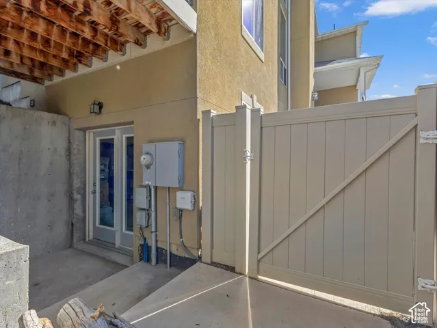 Concrete patio with direct access via a double glass door, featuring an overhead exposed wood beam structure and a light-colored privacy fence with a secure latch