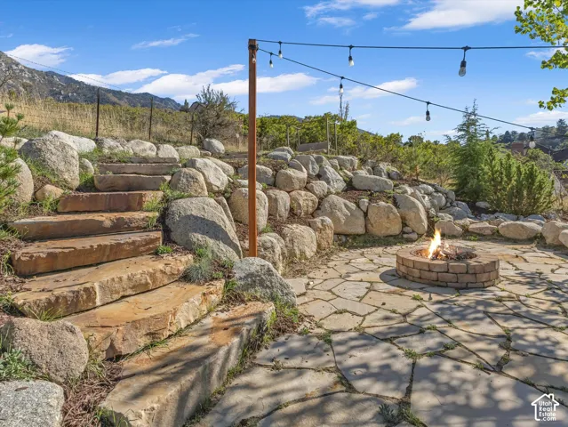 Stone patio with a built-in fire pit, string lighting, natural stone steps, and a rock retaining wall