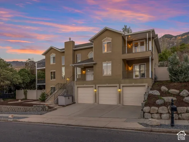 Multi-level stucco exterior with three garage bays, multiple balconies, and exterior staircases