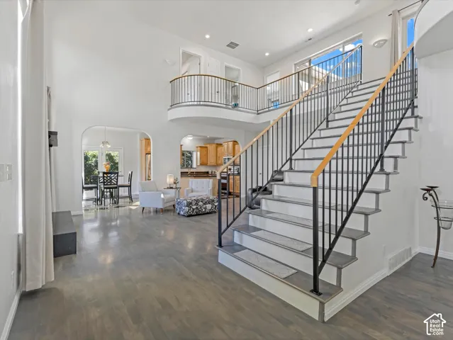 Double-height ceiling, wood-finish flooring, wrought iron staircase with wood handrail, open archways, and upper-level balcony