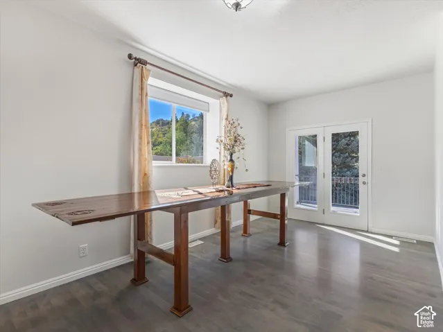 Bright dining room featuring dark wood-finish flooring, a solid wood dining table with turned legs, and abundant natural light from dual windows