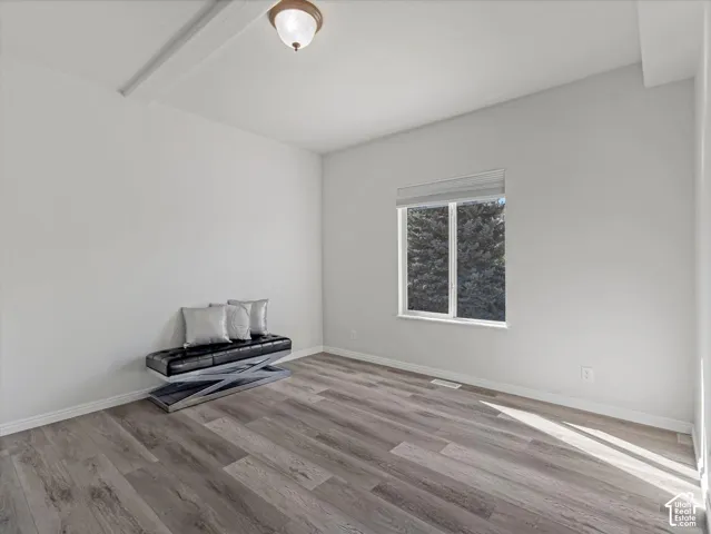 Recessed window with roller shade, wood-finish flooring, white baseboards, and ceiling-mounted light fixture