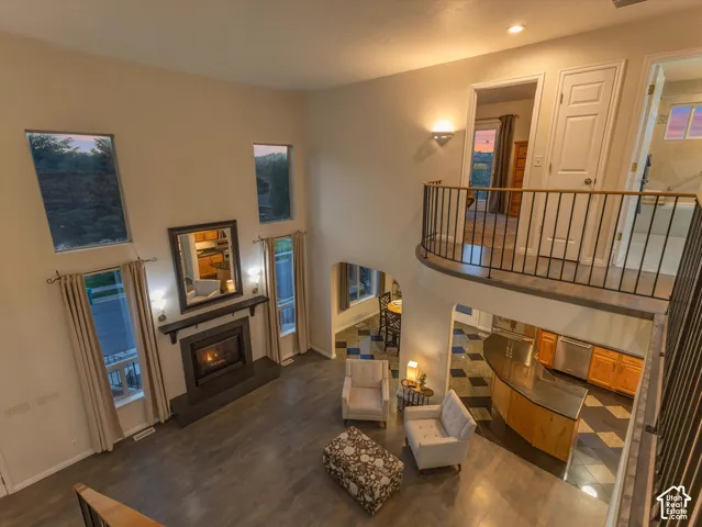 Two-story ceiling with high windows, built-in fireplace, wood-finish flooring, second-story landing with metal railing, and a kitchen with an island and checkerboard tile flooring