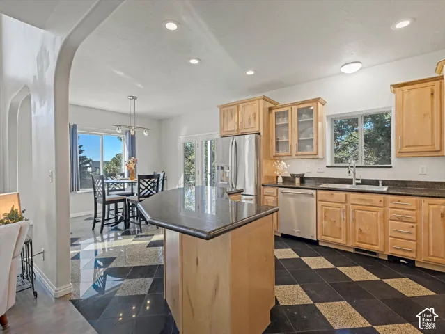 Kitchen featuring natural wood cabinetry, stainless steel appliances, dark stone countertops, and a central island with a matching stone surface