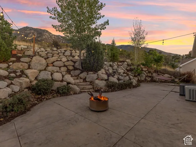 Stamped concrete patio featuring a built-in fire pit, string lighting, and a tiered rock retaining wall with integrated steps