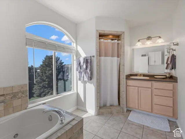 Arch-top window with blinds, large built-in tub with tile surround, walk-in shower with tile surround, vanity with built-in cabinetry, and tile flooring