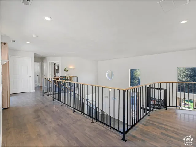 Upper landing with recessed lighting, wood-finish flooring, black metal railings, and a circular window
