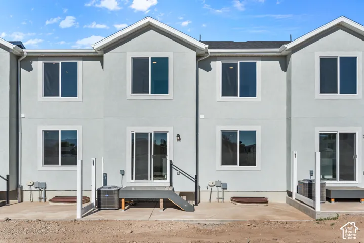 Rear exterior featuring a concrete patio, multiple windows, and a sliding glass door