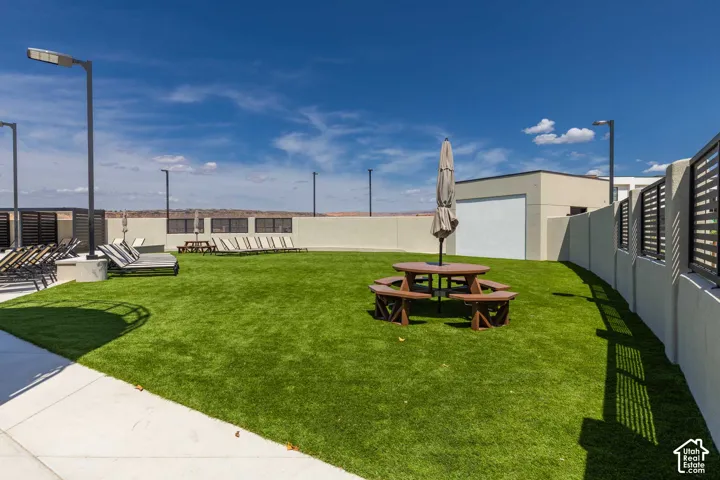 Rooftop outdoor space featuring artificial turf, a picnic table with umbrella, lounge chairs, and perimeter fencing