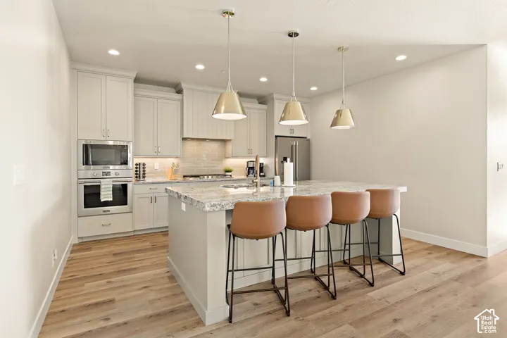 Kitchen featuring light cabinetry, stainless steel appliances, a center island with a stone-finish countertop, and wood-finish flooring