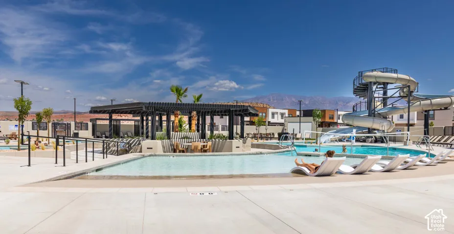 Resort-style pool area featuring a large water slide, shaded pergola, multiple lounge seating areas, and a zero-entry pool