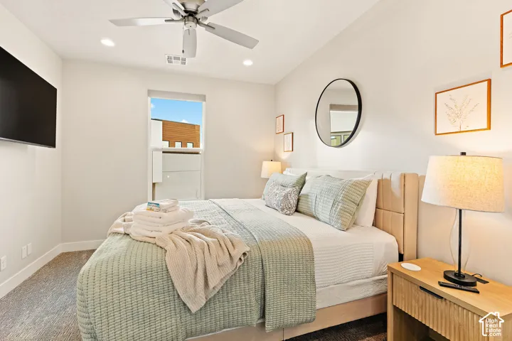 Recessed lighting, ceiling fan, wall-mounted television, neutral wall color, and textured bed frame