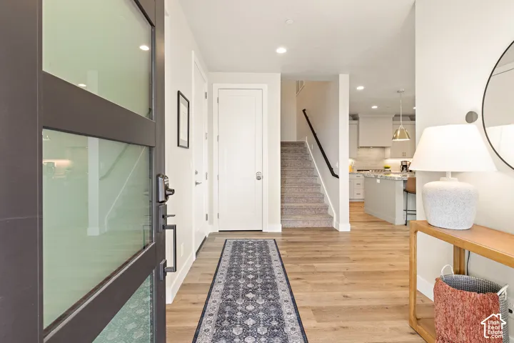 Wood-finish flooring, staircase with carpeted treads and black handrail, modern kitchen with white cabinetry and island