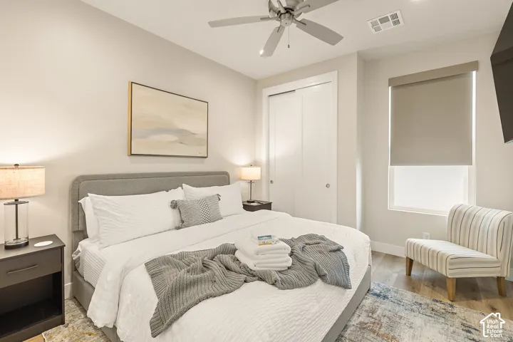 Recessed lighting, wood-finish flooring, sliding closet doors, window with roller shade, and ceiling fan with lighting