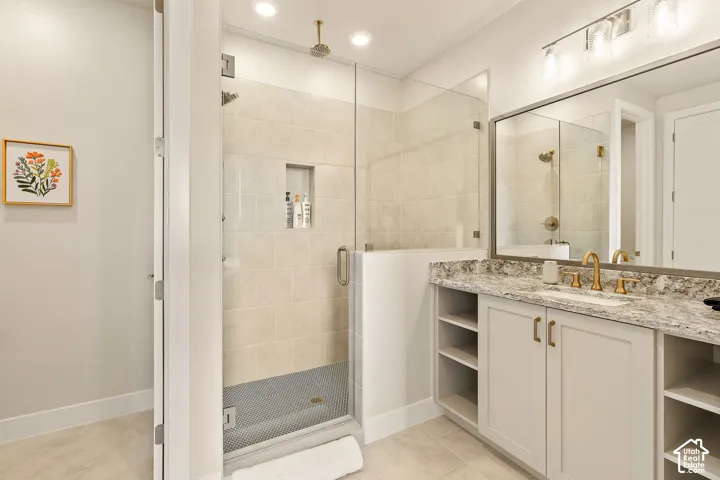 Glass-enclosed shower with a tiled surround and recessed shelf, vanity with a light-toned countertop, integrated sink, and gold-finish fixtures