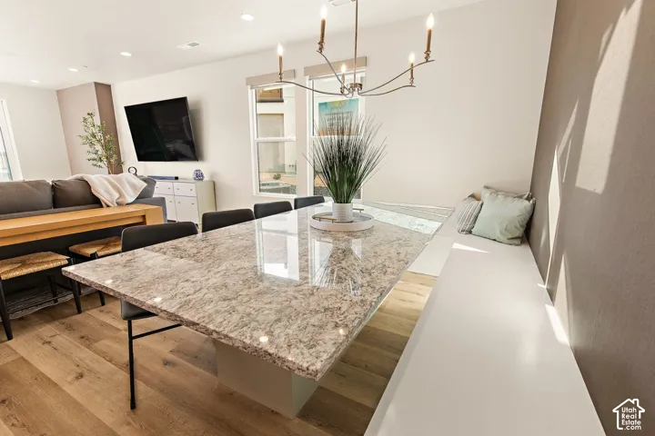 Spacious dining area featuring wood-finish flooring, a built-in bench, a chandelier, and a large dining table with a polished stone-finish surface