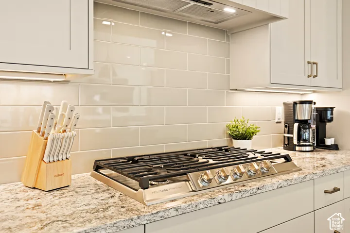 Built-in gas cooktop, under-cabinet lighting, light-toned cabinetry, subway tile backsplash, and speckled countertop