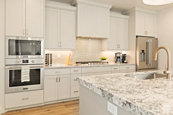Light-toned cabinetry, stainless steel appliances, speckled stone countertops, wood-finish flooring, and a subway tile backsplash