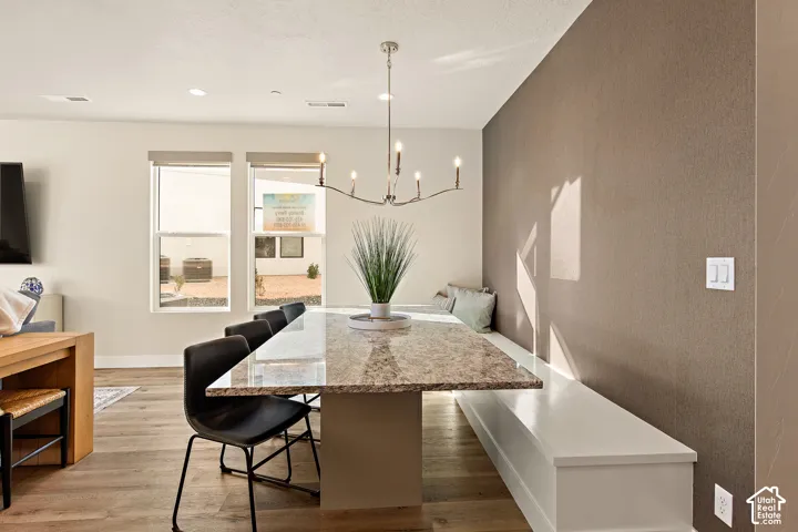Recessed lighting, wood-finish flooring, built-in bench seating, two large windows, and a linear chandelier