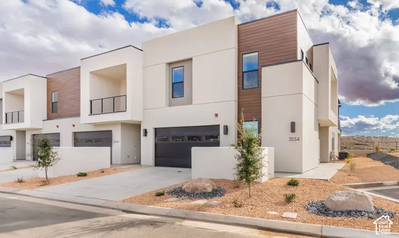 Contemporary exterior featuring light stucco, wood-finish siding accents, black garage doors, and xeriscaped landscaping