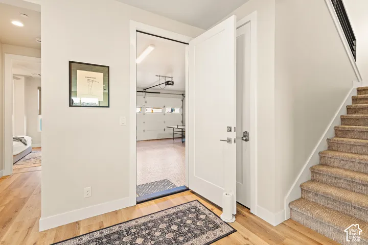 Wood-finish flooring, white interior doors with contemporary hardware, carpeted staircase, and a garage with overhead lighting