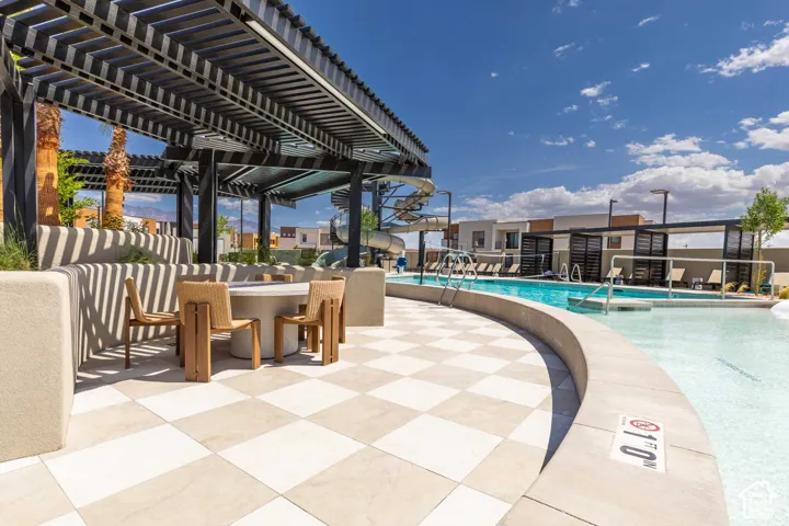 Resort-style pool area featuring checkered paver flooring, a large swimming pool, a water slide, and shaded lounge areas with pergolas