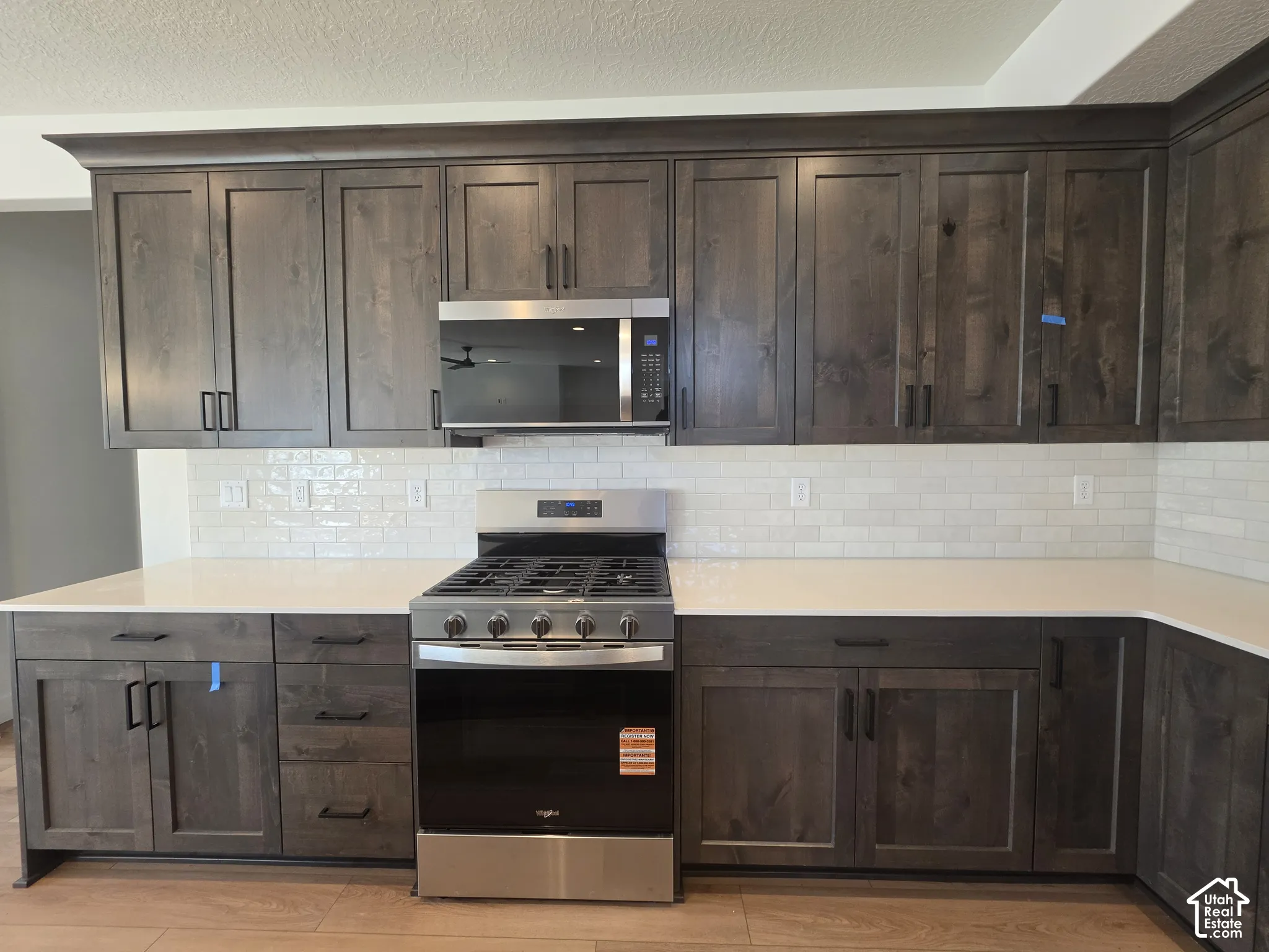 Dark wood-finish cabinetry, white subway tile backsplash, white countertops, stainless steel range, and wood-finish flooring