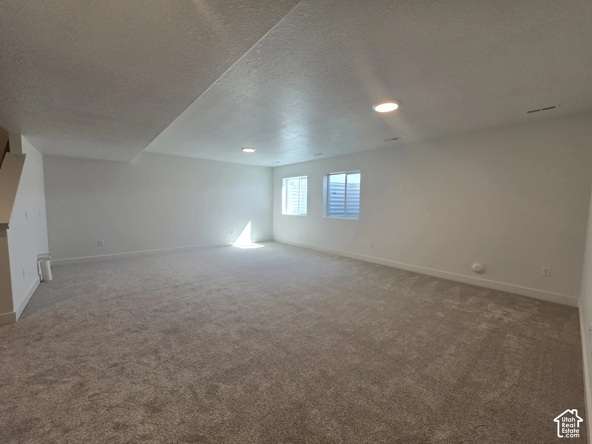 Spacious room featuring neutral carpeting, recessed lighting, and two windows with blinds
