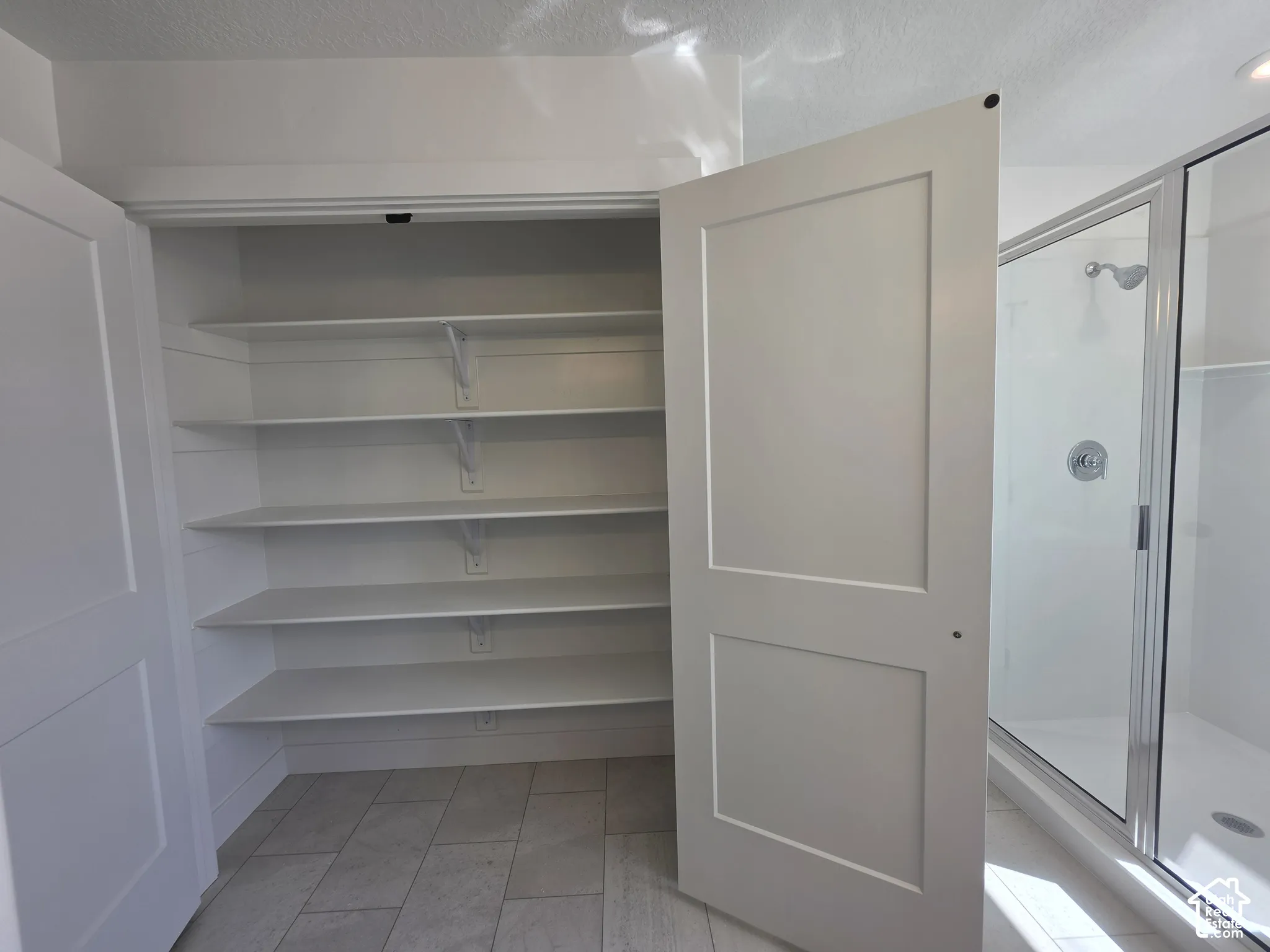 Built-in shelving, white two-panel doors, tiled flooring, glass-enclosed shower, and chrome shower fixtures