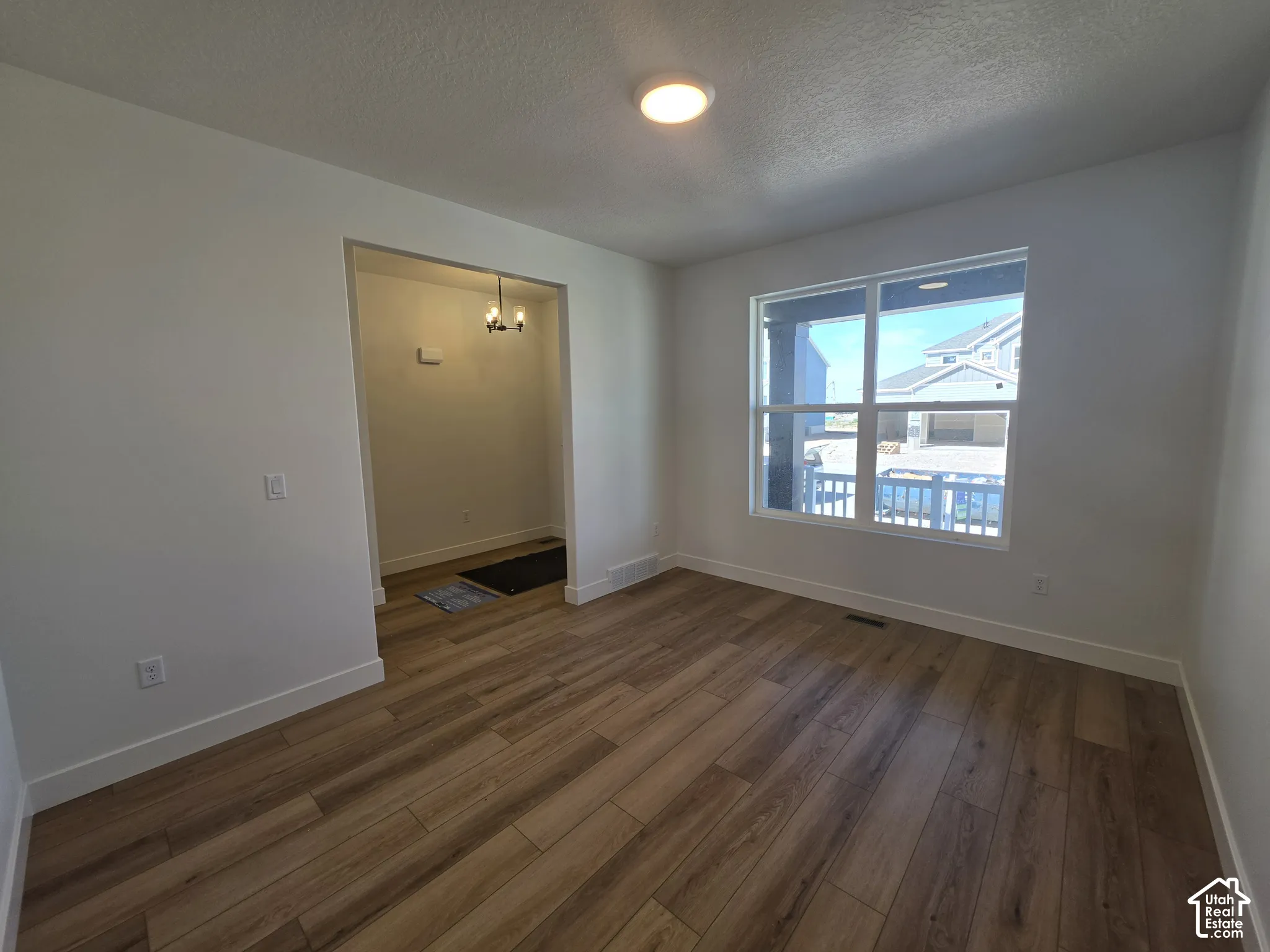 Wood-finish flooring throughout, bright white walls, large window, and an overhead light fixture