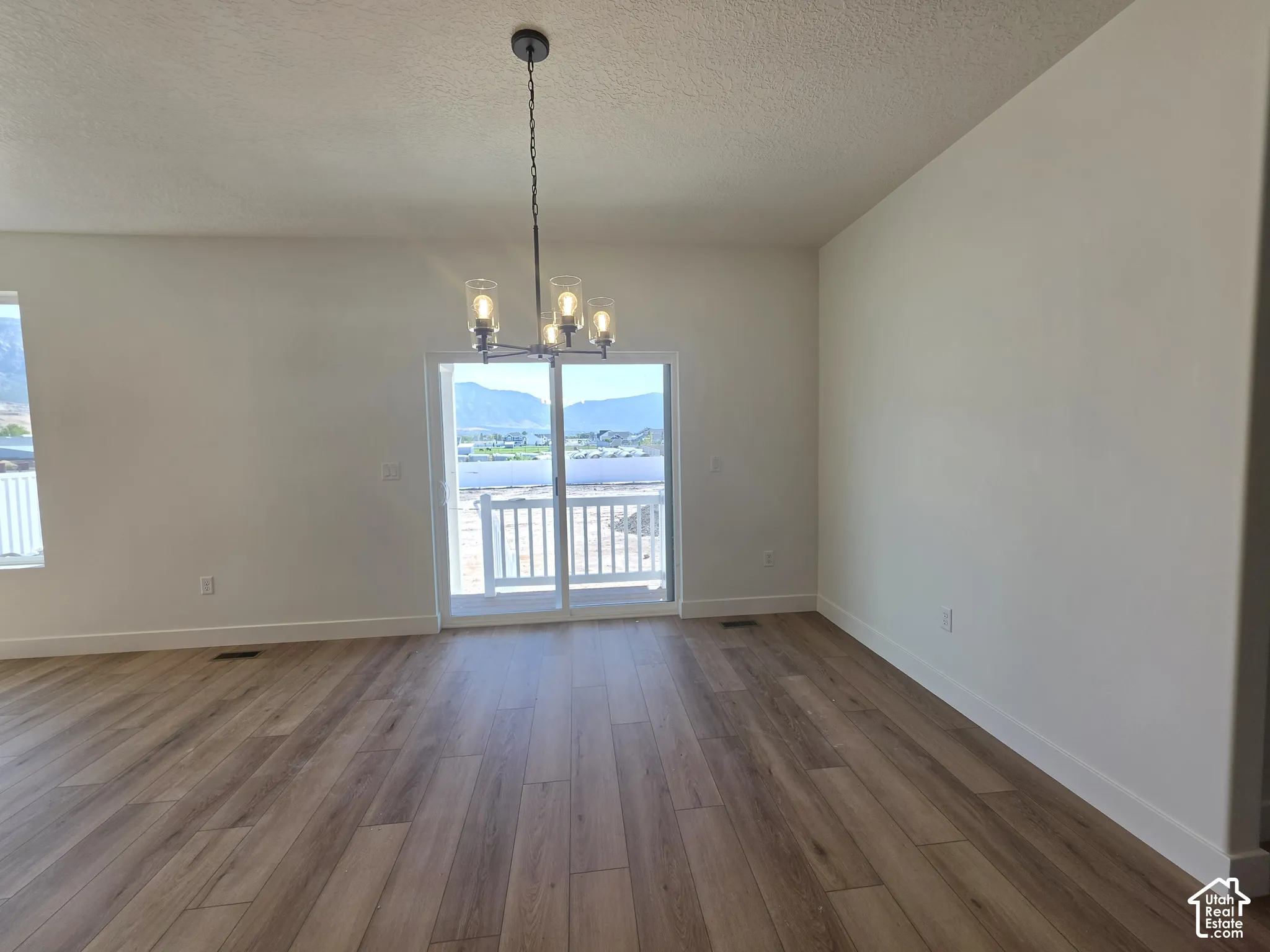 Spacious interior with wood-finish flooring, a modern chandelier, and white walls