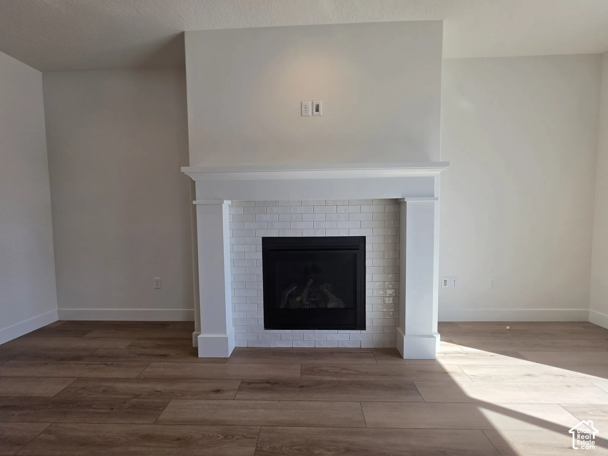 Fireplace with white subway tile surround, classic white mantel, and wood-finish flooring