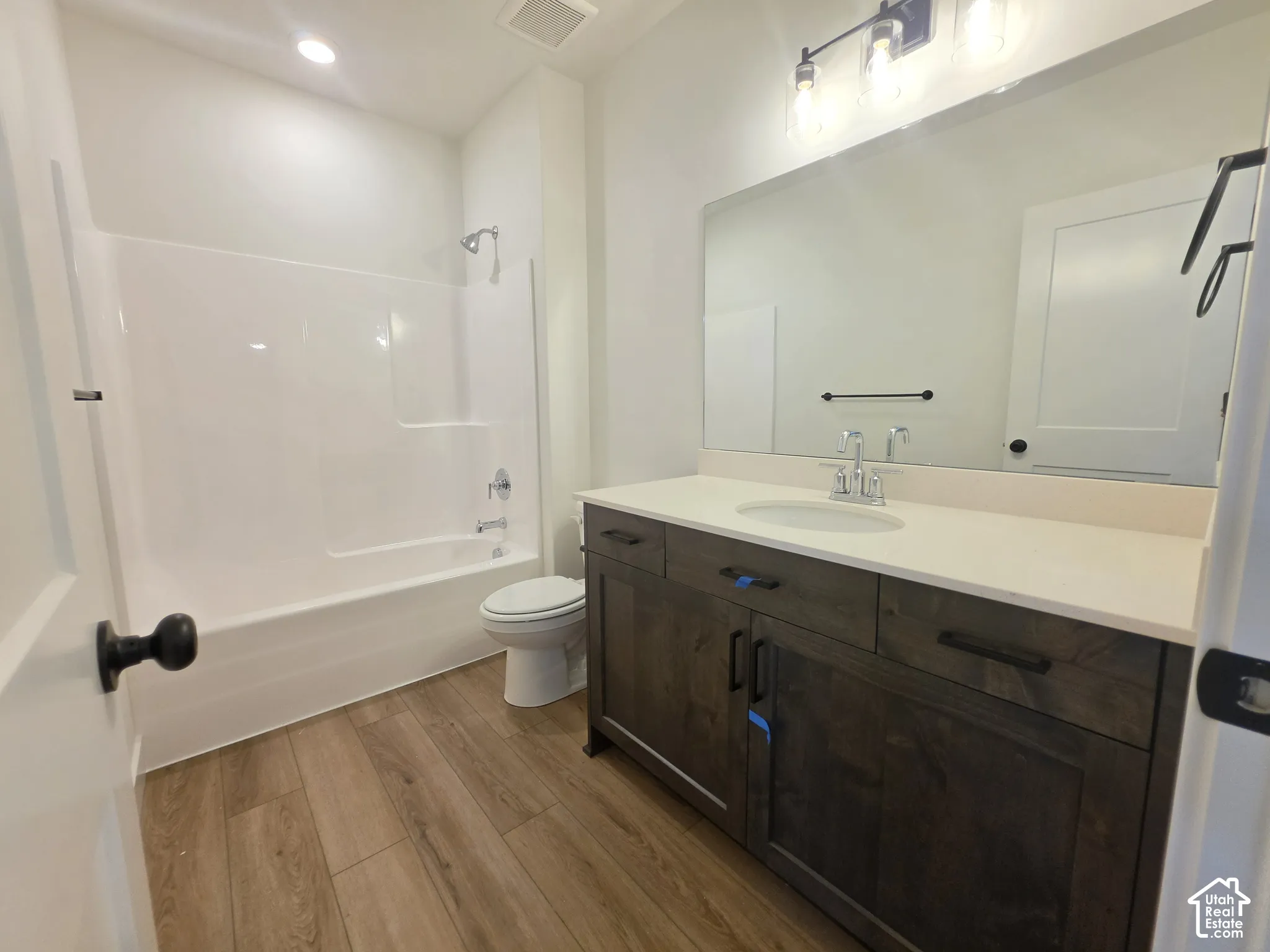 Bathroom featuring a single-piece tub and shower, wood-finish flooring, dark wood-tone vanity, light countertop, and a vanity mirror