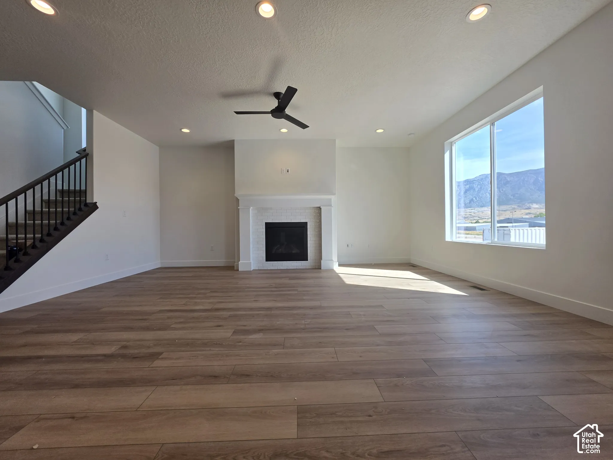 Spacious living area featuring wood-finish flooring, a contemporary ceiling fan, recessed lighting, and a white tile fireplace with a mantel