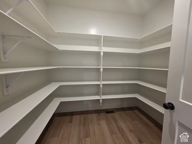 Walk-in pantry featuring expansive white shelving, wood-finish flooring, and a white interior door with black hardware