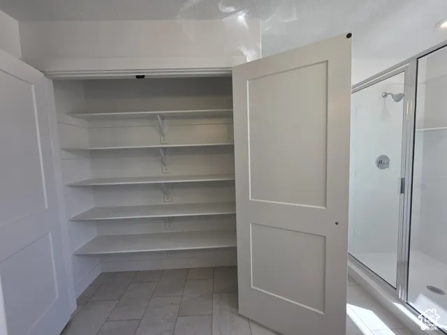 Built-in shelving, white two-panel doors, tiled flooring, glass-enclosed shower, and chrome shower fixtures