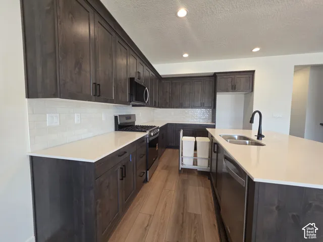 Kitchen featuring wood-finish flooring, dark wood cabinetry, white countertops, a subway tile backsplash, and a stainless steel sink with a matte black faucet