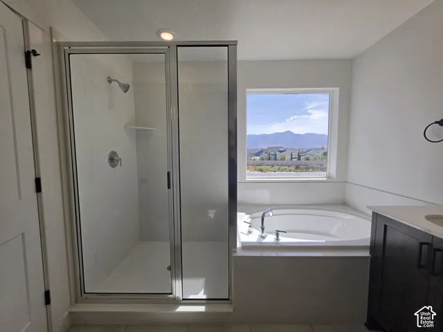 Built-in soaking tub, separate glass-enclosed shower, single vanity with dark wood cabinetry, and a large window