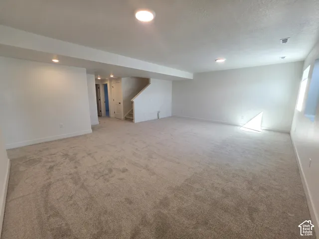 Expansive finished room with light-toned carpeting and white walls