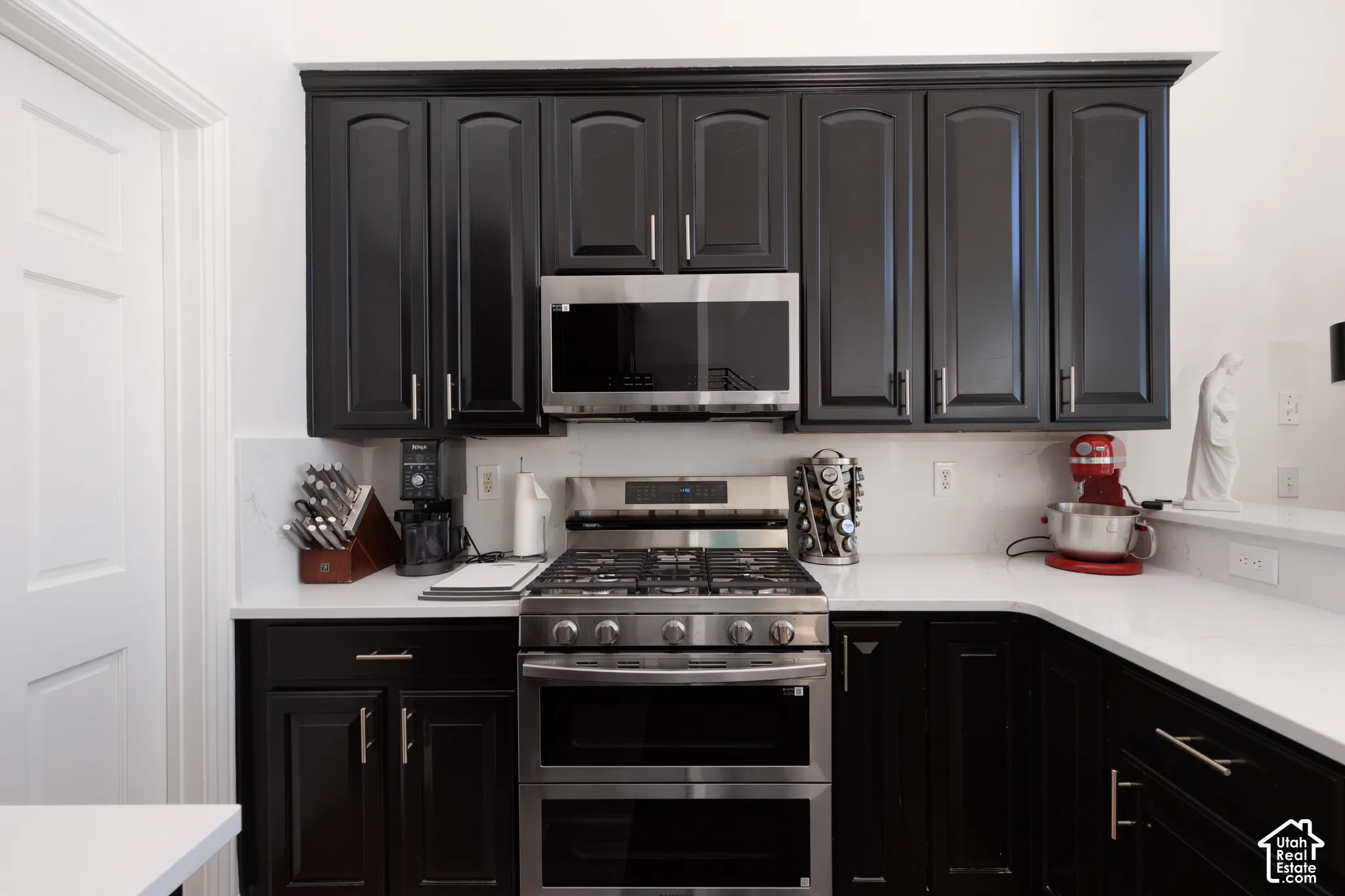 Black cabinetry with brushed nickel hardware, stainless steel gas range with double oven, built-in microwave, white countertops, and white tile backsplash