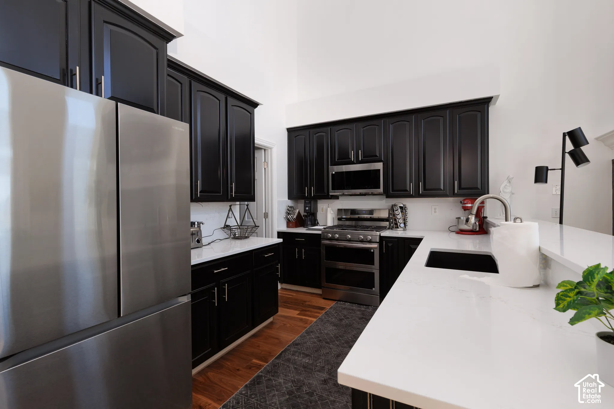Vaulted ceiling kitchen featuring black cabinetry, stainless steel appliances, white countertops, and wood-finish flooring
