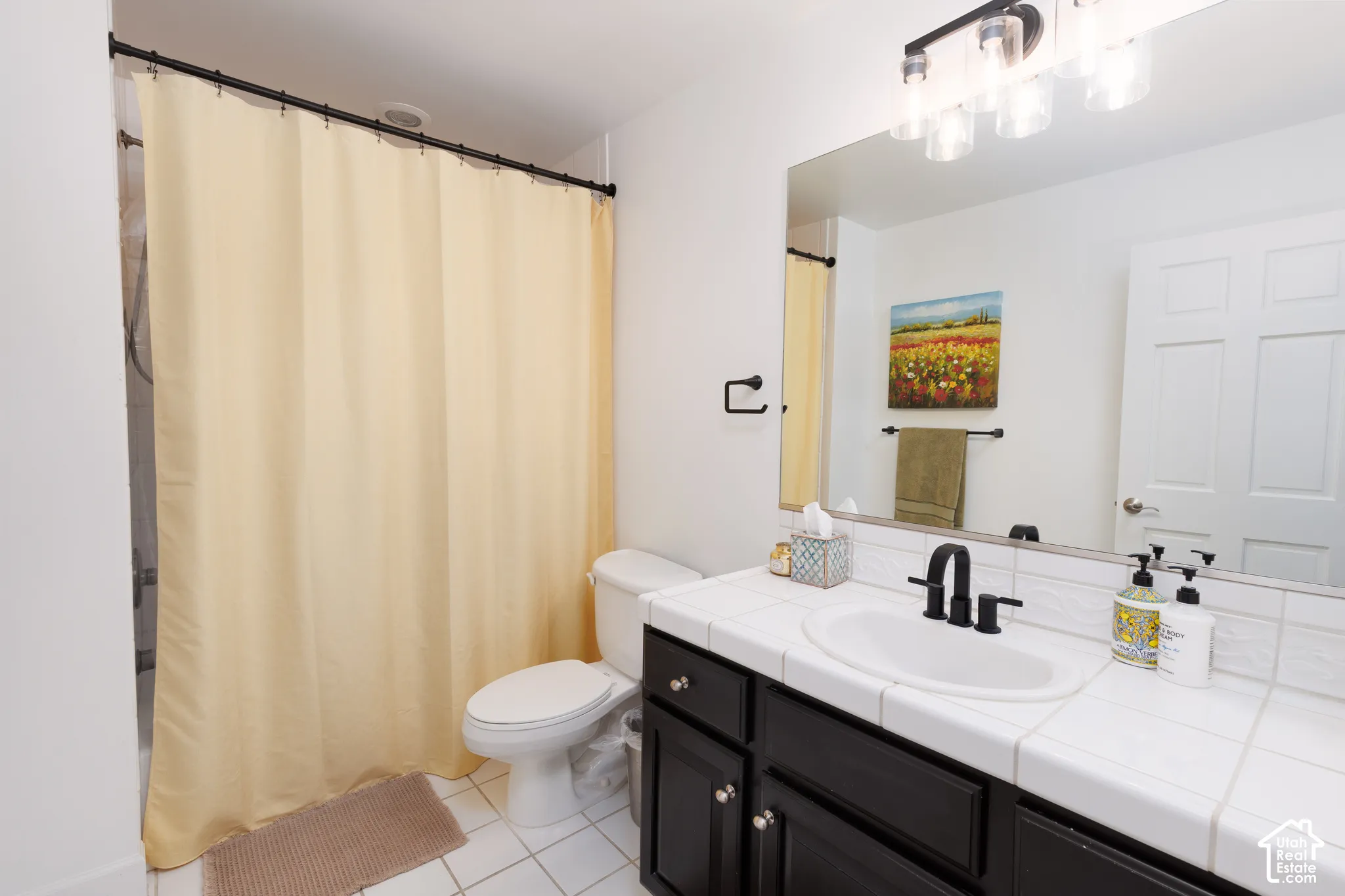 White tiled flooring, dark wood-finish vanity with silver hardware, white tiled countertop, undermount sink, and matte black faucet