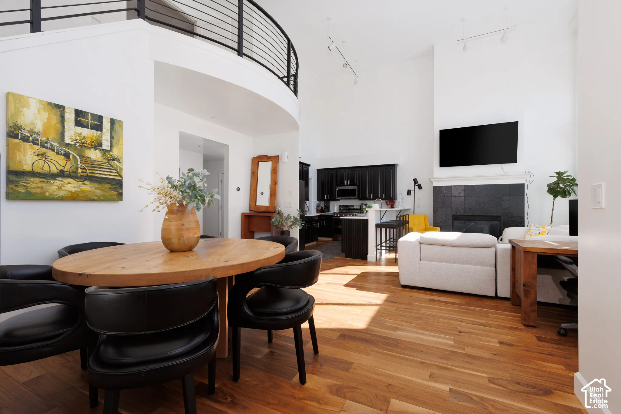 Vaulted ceilings, wood-finish flooring, fireplace with dark tile surround, and an open loft with a metal railing