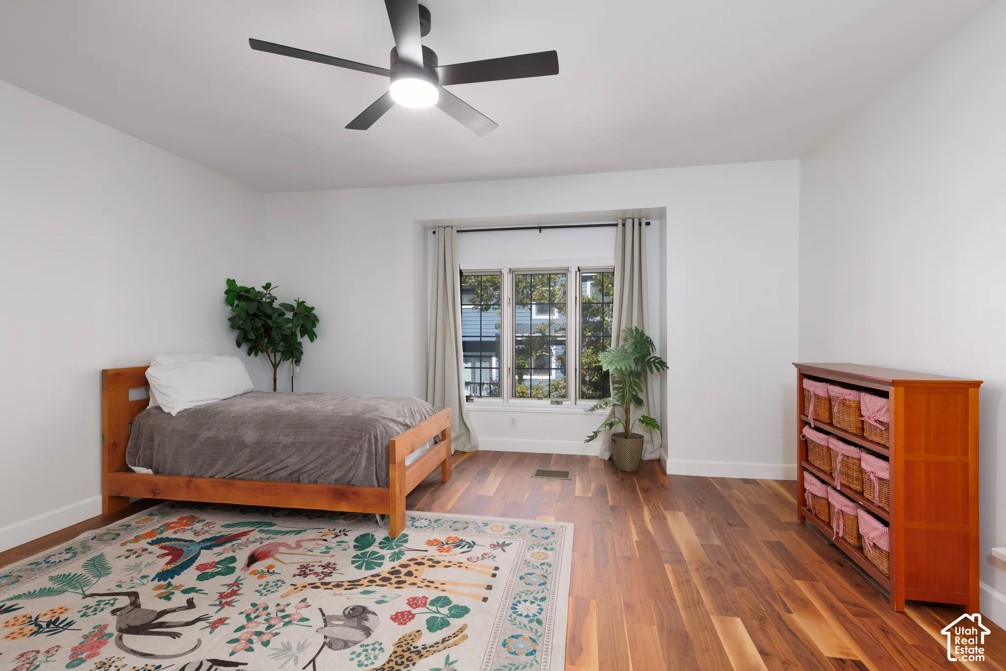 Spacious room featuring wood-finish flooring, a contemporary ceiling fan with integrated lighting, and a window with a dark frame
