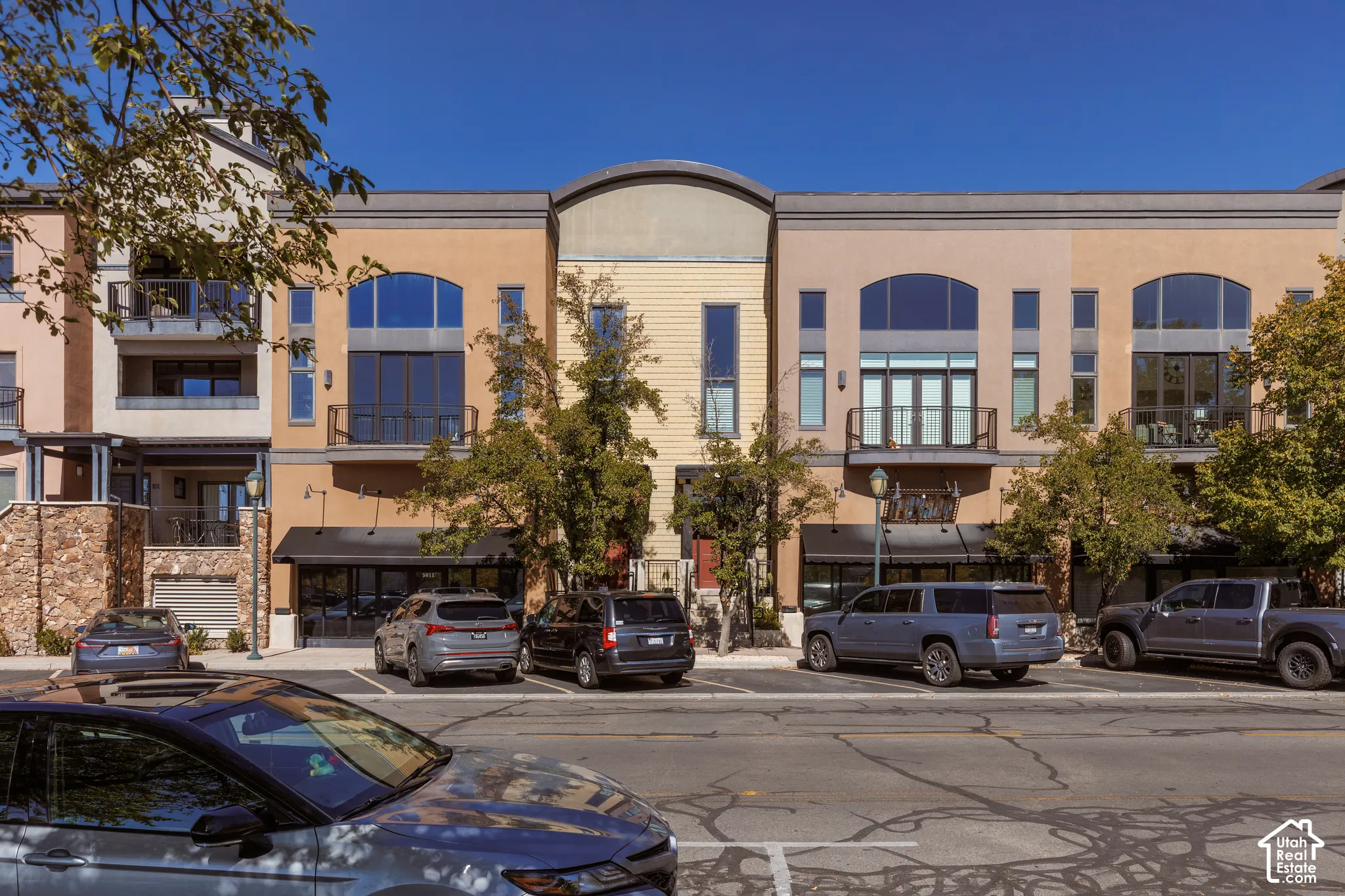 Multi-level building exterior featuring multiple balconies, large arched windows, and ground-floor retail space with awnings