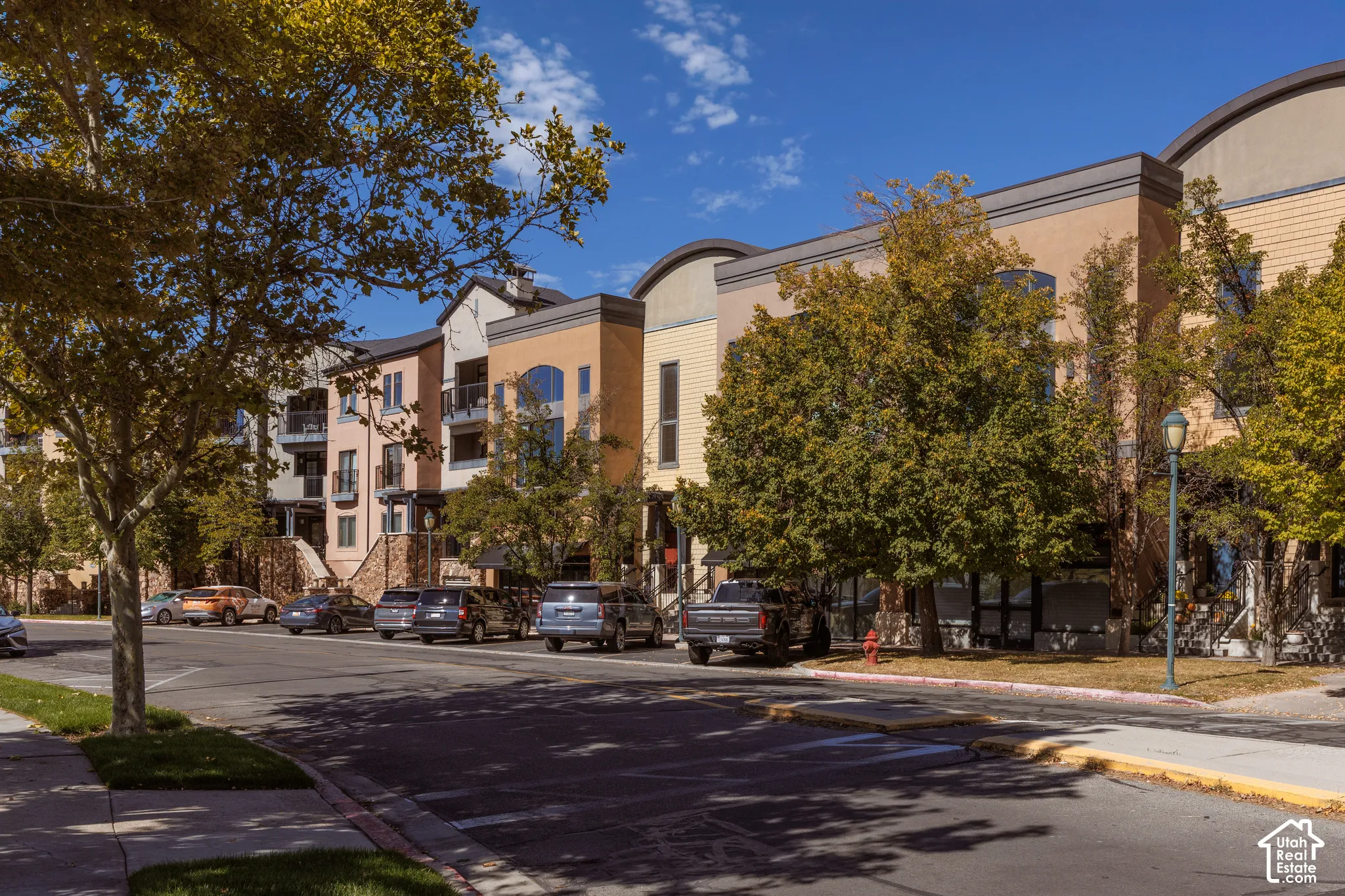 Multi-story residential facade featuring balconies, varied exterior finishes, and mature trees